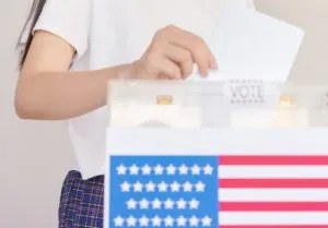Woman placing voting ballot into box with American flag design