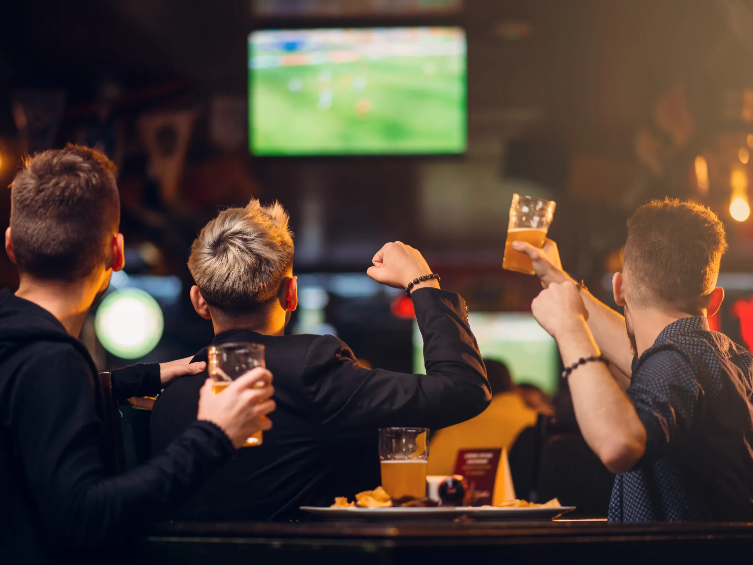 group of men watching sports at a bar and raising glasses