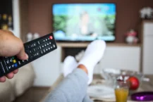 2024 TV Advertising Trends - person pointing remote at TV in the background with legs kicked up on coffee table