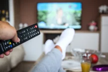 TV Advertising Advantages - person pointing remote at TV in the background with legs kicked up on coffee table