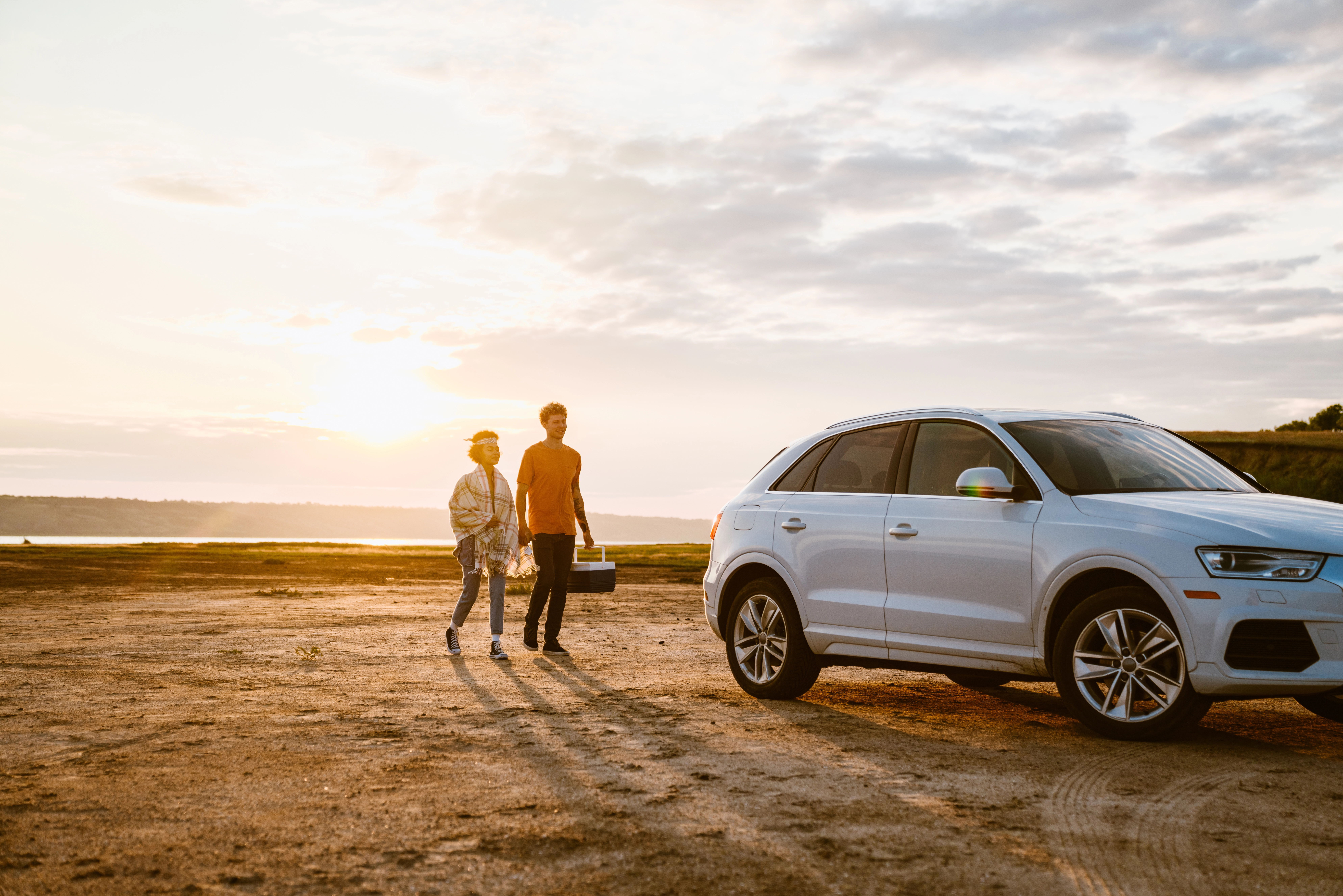 couple walks along beach at sunset with car